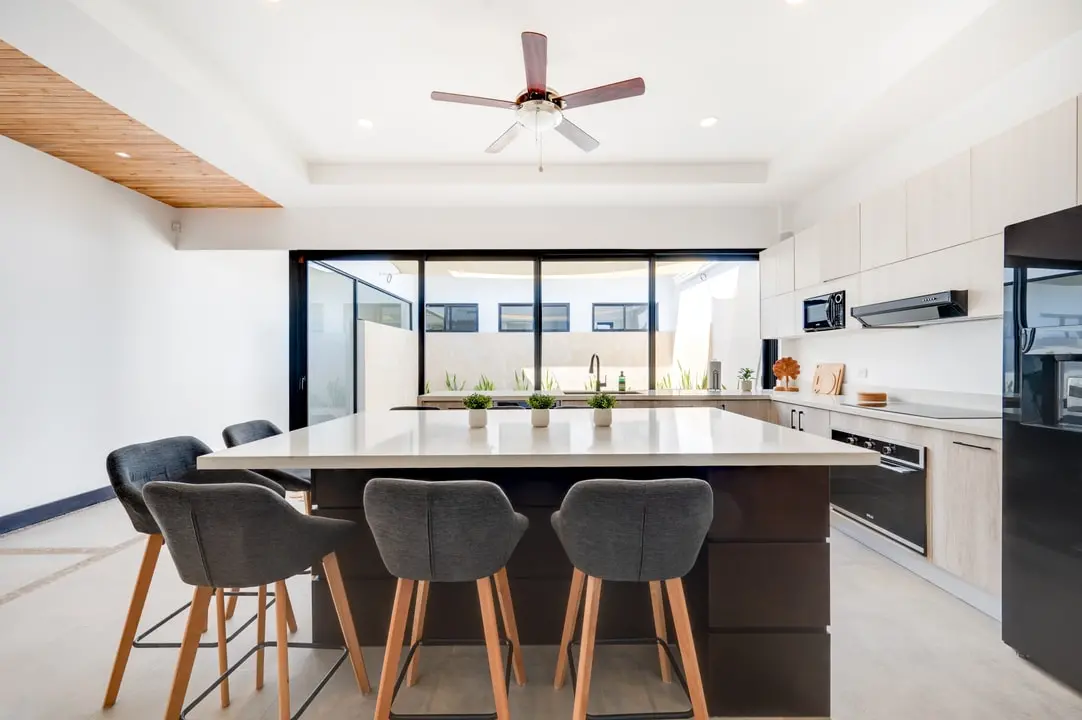 Tamawalk's kitchen features a central island with comfortable chairs, high-end appliances, light wood cabinetry, and a minimalist design.