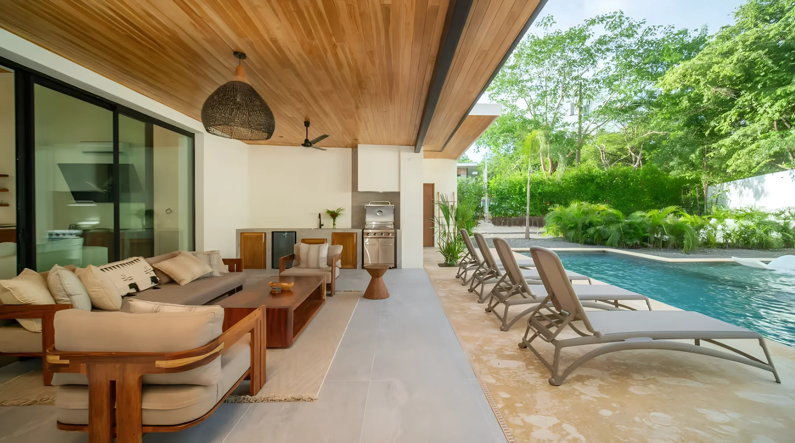 Renderizado del interior del área social de la Casa CM, con un diseño contemporáneo que destaca por el techo de madera, ventanales de piso a techo y una distribución abierta que integra sala, comedor y cocina. Los acabados cálidos y naturales brindan confort, elegancia y una conexión visual con el jardín exterior.