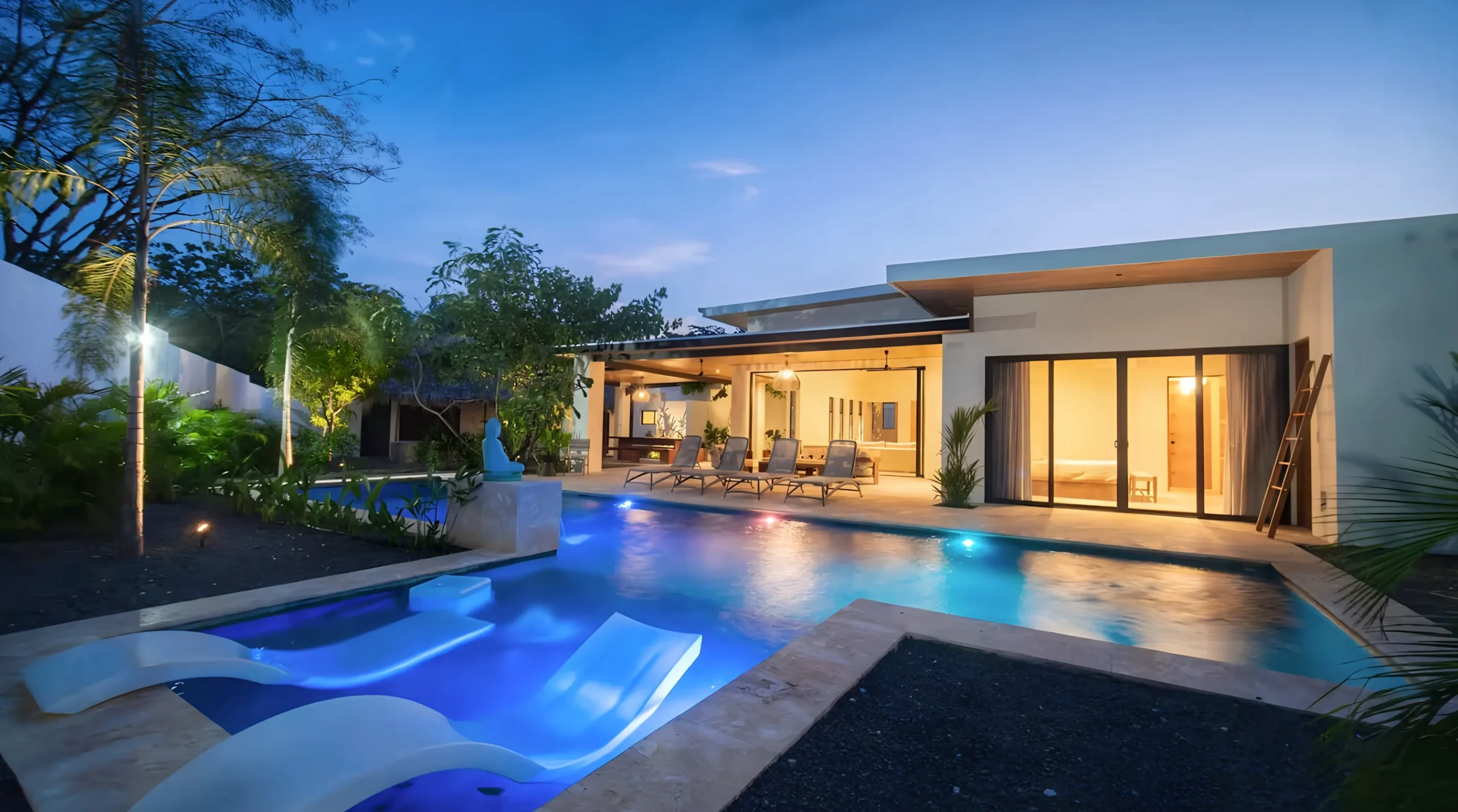 House Corona's backyard features a lighted pool, surrounded by gardens and outdoor relaxation areas.