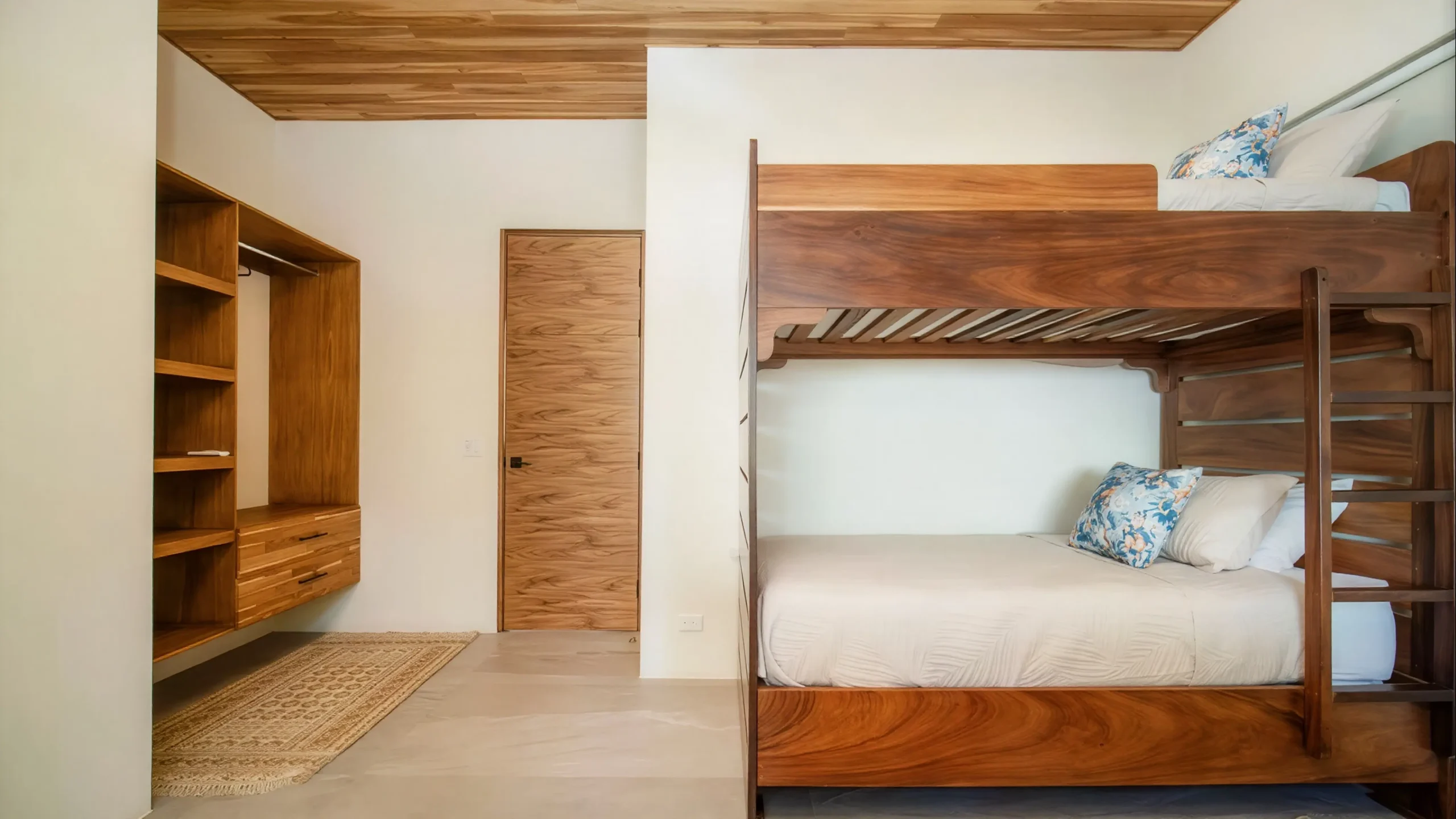 A versatile room at House Corona, featuring a handcrafted wooden bunk bed and a minimalist design. It includes a built-in wardrobe and a decorative rug.